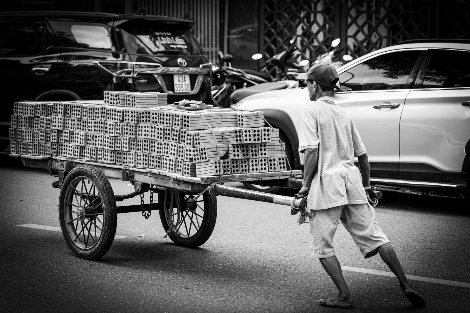 Man pulls a cart filled with bricks on a road.