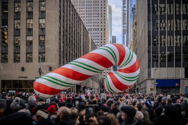 Giant candy cane balloon floats over a city street parade.