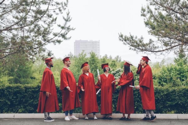 Graduates in red gowns stand together outdoors.